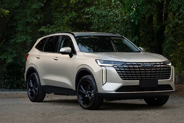 A beige Haval SUV parked outdoors with green trees in the background.