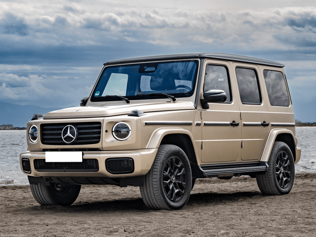 A beige Mercedes-Benz G-Class SUV parked on a sandy beach by the water.