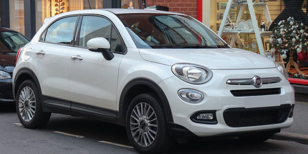 A white Fiat car parked on the street in front of a store with festive decorations.