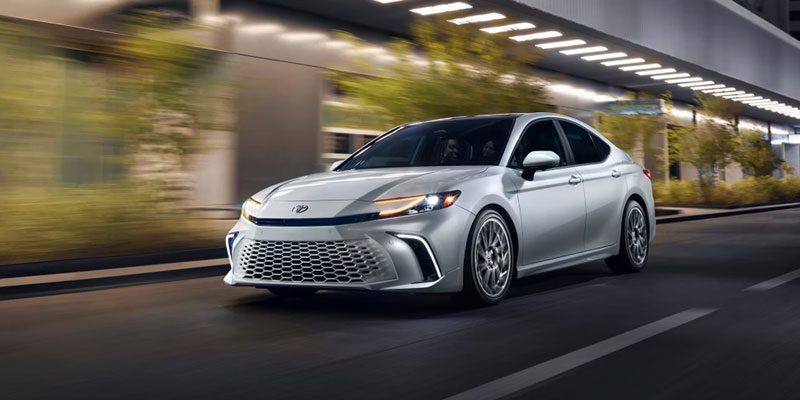 A silver Toyota sedan driving on a city road at night, with blurred urban scenery, highlighting its sleek design and dynamic performance.