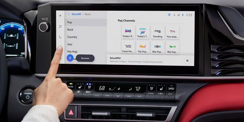 A hand interacting with a car’s infotainment screen displaying SiriusXM music channels (Pop, Rock, etc.), alongside a digital dashboard with vehicle stats, showcasing the intuitive in-car entertainment system.