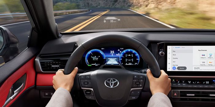 Interior view of a Toyota car, showing a driver’s hands on the steering wheel, digital dashboard with speed (35), infotainment screen, and a road ahead with adaptive cruise control display.