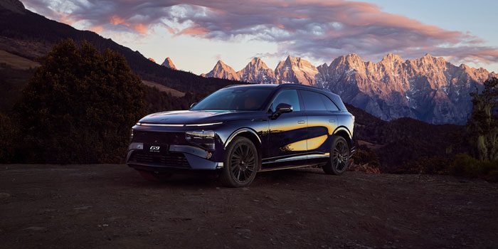 A dark blue SUV parked on a rocky terrain, with majestic mountains and a colorful sunset sky in the background, highlighting its sleek design and scenic surroundings.