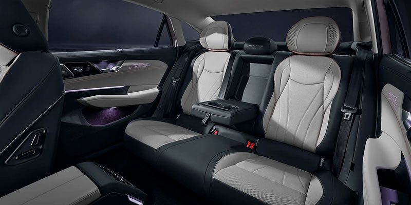 Rear interior of a car with black and gray leather seats, ambient lighting, and a central armrest, emphasizing a luxurious and comfortable design.