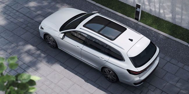 Aerial top-down view of a white Volkswagen wagon: Shows sleek estate body, large sunroof, and alloy wheels. Parked on paved ground near greenery, highlighting its modern, practical design.