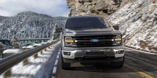 2026 Ford F-150 Lariat being driven on a mountain roadway with snow covered mountains