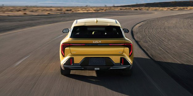 2026 Kia K4 Hatchback, accelerating down a curving desert road, rear-view