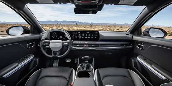 Interior full-view of the 2026 Kia K4 Hatchback's front row seats, digital display, and steering wheel, with the desert terrain visible through the windshield
