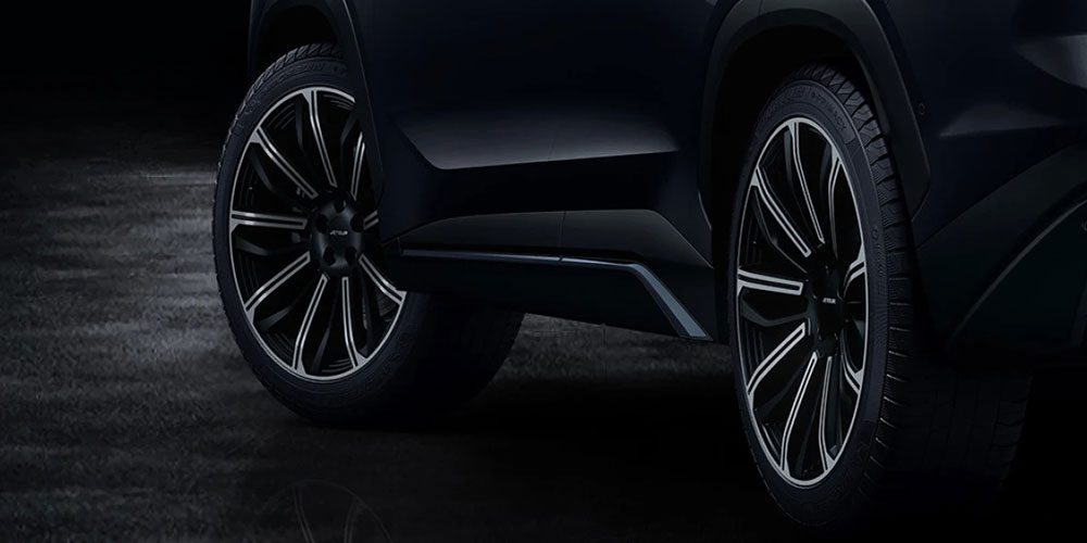 Close-up of a black SUV’s wheels: sleek multi-spoke rims with silver accents, dark body panel, dim background.