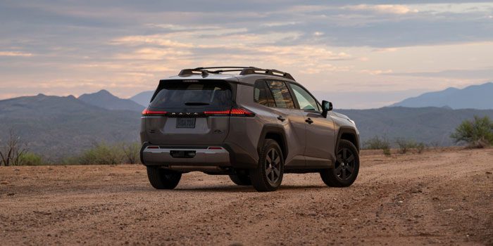 Gray Toyota SUV parked on a desert dirt road, showcasing its rear design against a backdrop of mountains and a sunset sky.