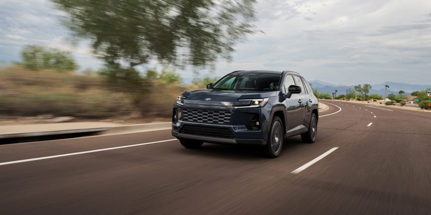 Dark blue SUV driving dynamically on a sunlit desert highway, with blurred roadside foliage emphasizing motion.