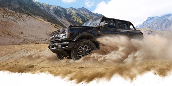 A 2026 Ford Bronco SUV kicking up dust in a valley beneath rocky hills