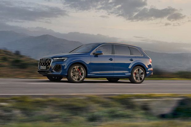 Audi SQ7 in motion: Vibrant blue performance SUV cruising on a scenic road with mountain backdrops at golden hour.