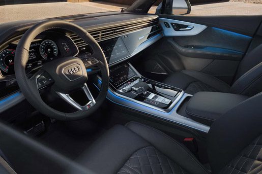 Audi Q7 interior: Sleek black cockpit with dual touchscreens, ambient blue lighting, and quilted leather seats.