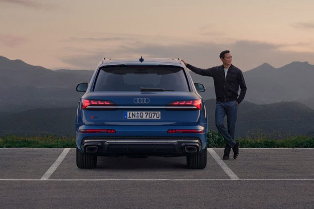 Audi Q7 rear view: Striking blue luxury SUV with signature OLED taillights, parked against a mountain sunset backdrop.