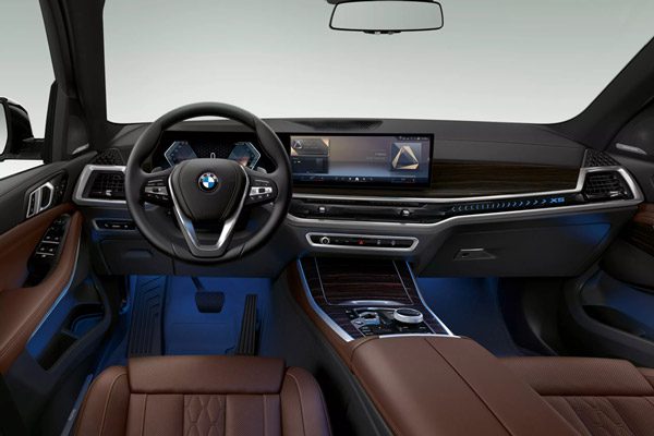 BMW X5 cockpit: Luxurious brown leather seats, curved infotainment screen, and ambient blue lighting.