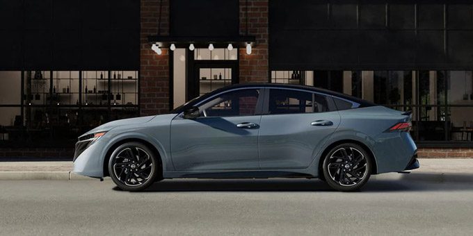 2026 Nissan Sentra side view parked in front of building with windows and subtle lighting at dusk.