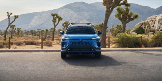 Blue Buick EV front view: Parked on a desert road with Joshua trees and mountain backdrops at sunrise.