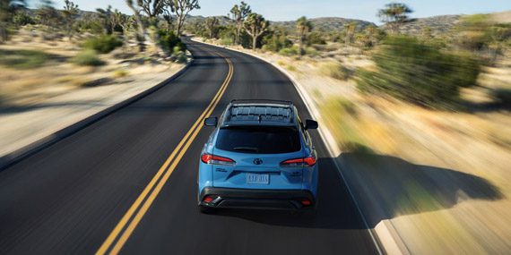 Toyota Corolla Cross: Light blue SUV cruising on a desert highway, surrounded by Joshua trees and rocky terrain.