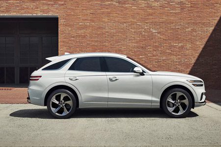 Side view of white Genesis GV70 parked in front of a brick wall