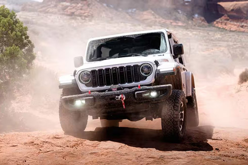 Front view of a white 2026 Jeep Wrangler driving in the sand